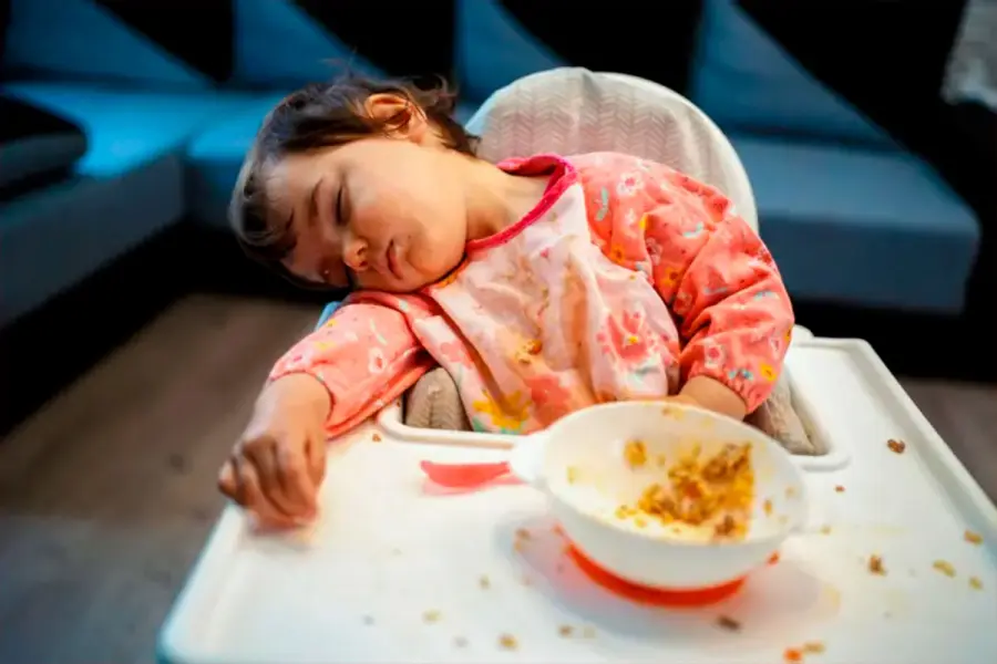 Ni&ntilde;a peque&ntilde;a dormida frente a su mesita de comer, con un bol pl&aacute;stico en el que se ven restos de comida. (Foto: Getty Images).