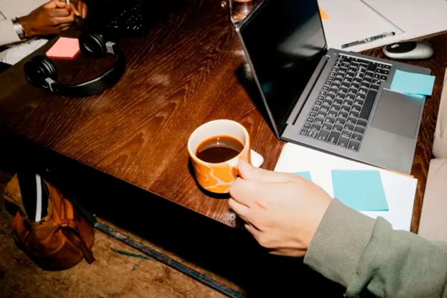 Vista de un hombre sosteniendo una taza de caf&eacute; junto a un port&aacute;til en el escritorio de una oficina. (Foto: Getty Images).